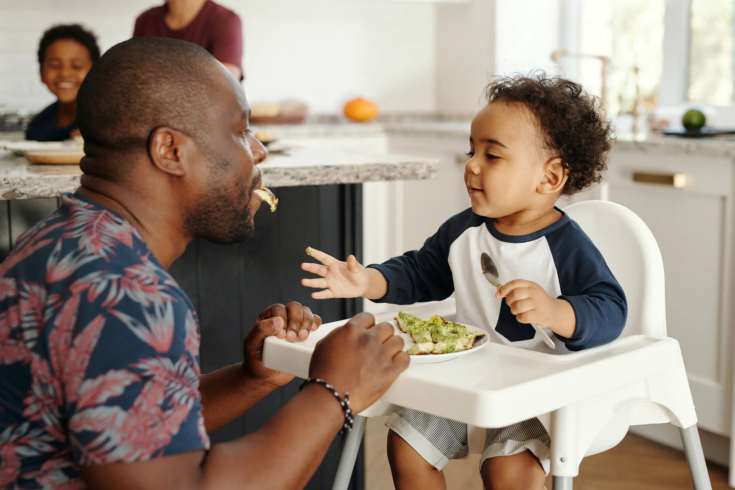 A man feeding his toddler in a high chair