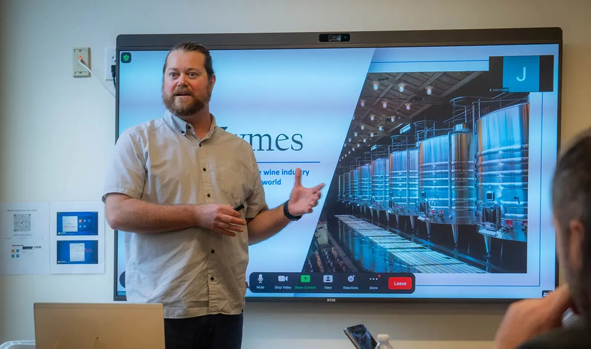 Man speaking at a meeting in front of a large tv screen